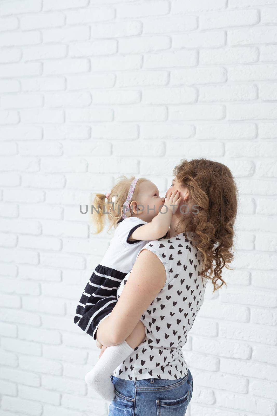 Mother holds her child with hearing aids and cochlear implants on white brick wall . Deaf and health concept by Satura86
