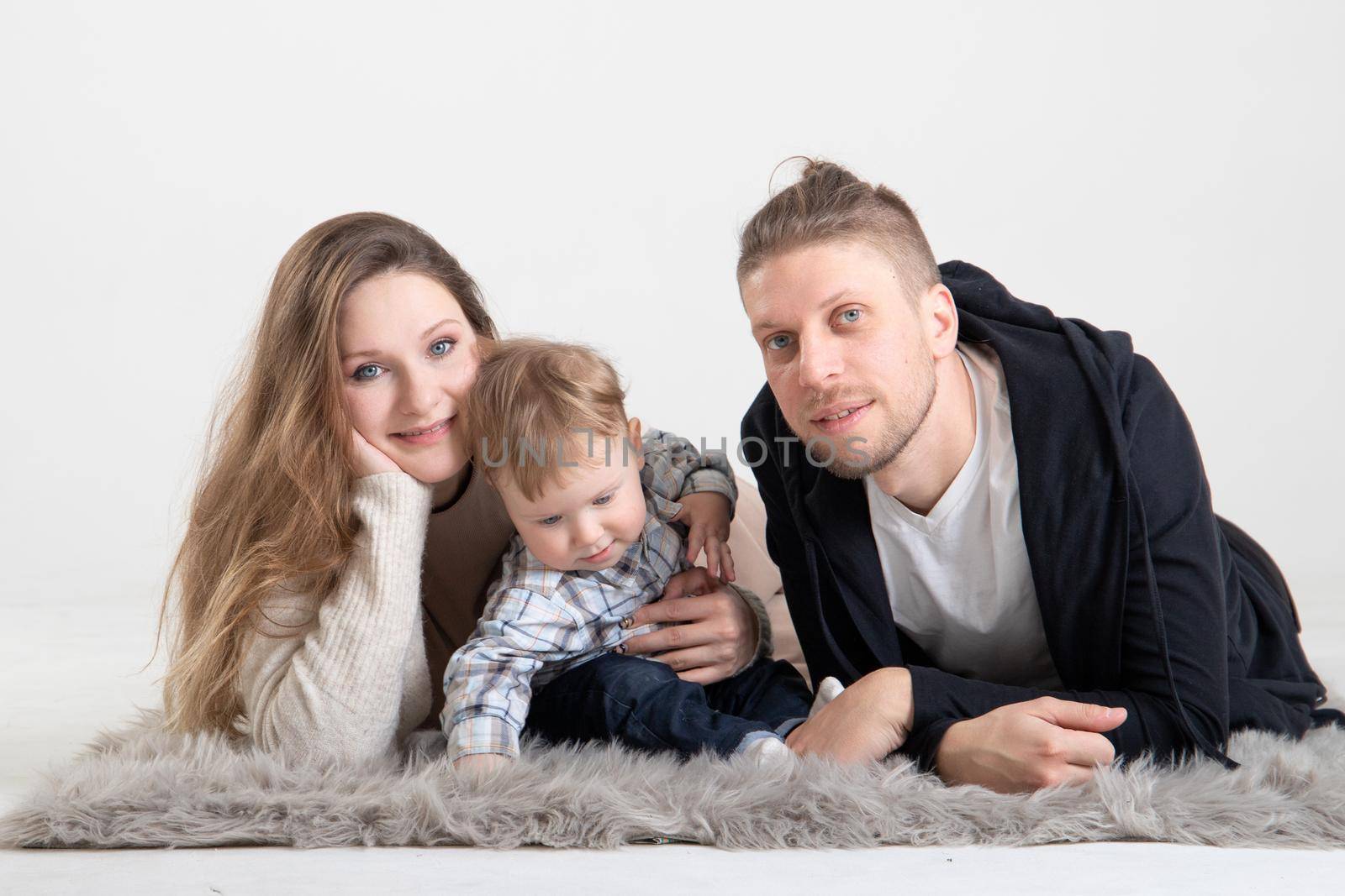 Portrait of young caucasian parents with one year old son on the floor on a white background.