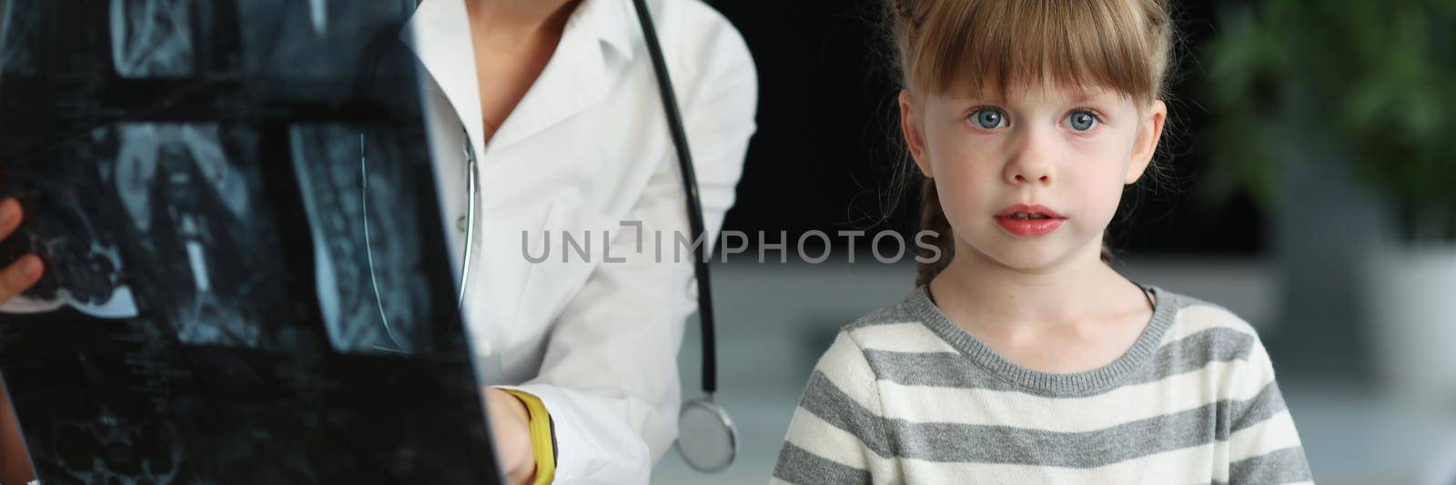 Cute woman doctor showing and explaining to daughter x ray result by kuprevich