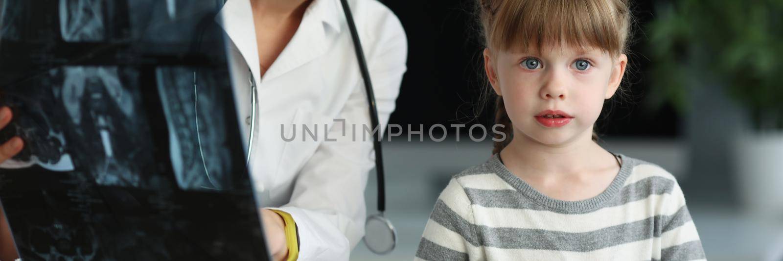 Portrait of cute woman doctor showing and explaining to daughter x ray result. Child visit mum at work in hospital. Medicine, childhood, parenthood concept