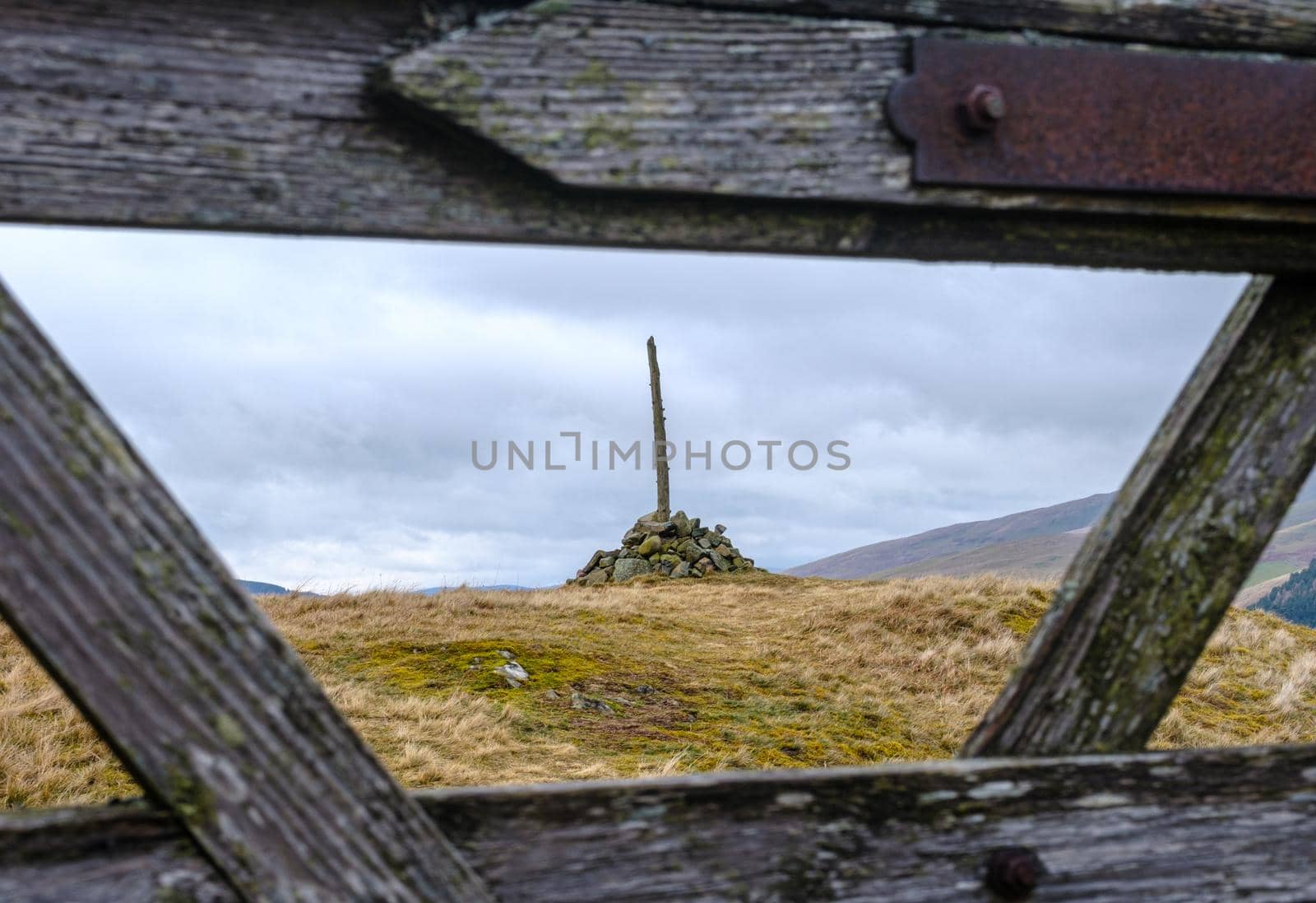 A Cairn (Pile or Stack of Stones) To Mark The Summit Of A Hill In Scotland Framed Through A Wooden Gate