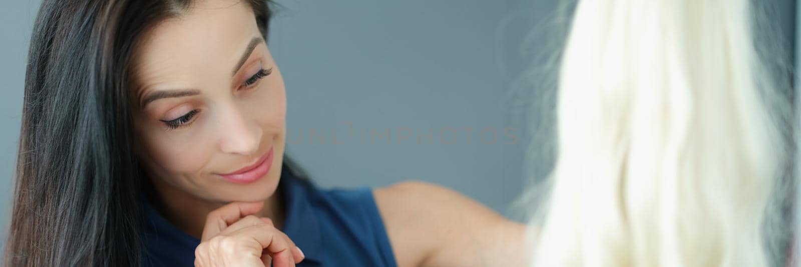 Portrait of brunette woman holding blonde wig with long hair and thinking to wear it. Change image for day, try on new things. Hairdresser haircare concept