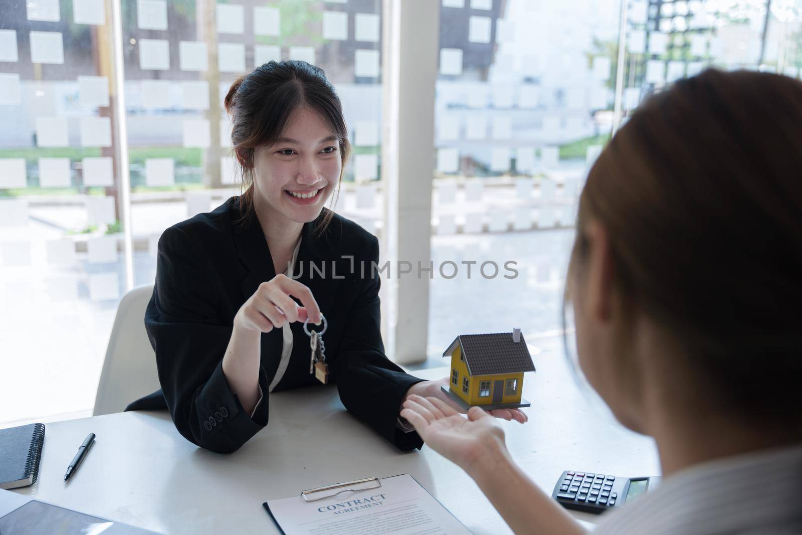 Accountant, businessman, real estate agent, Asian business woman handing key to customers along with house interest calculation documents for customers to sign