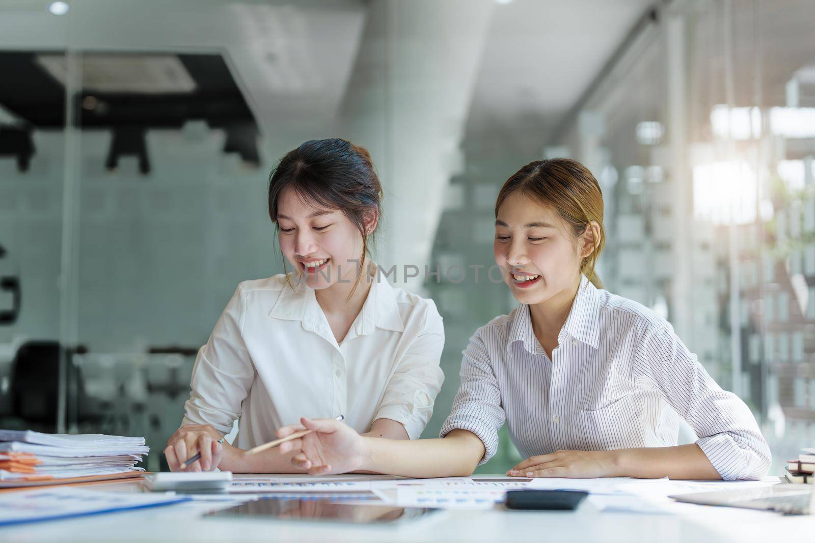 Negotiation, Analysis, Discussion, Portrait of an Asian young economist and marketer pointing to a financial data sheet to plan investments to prevent risks and losses for the company. by Manastrong