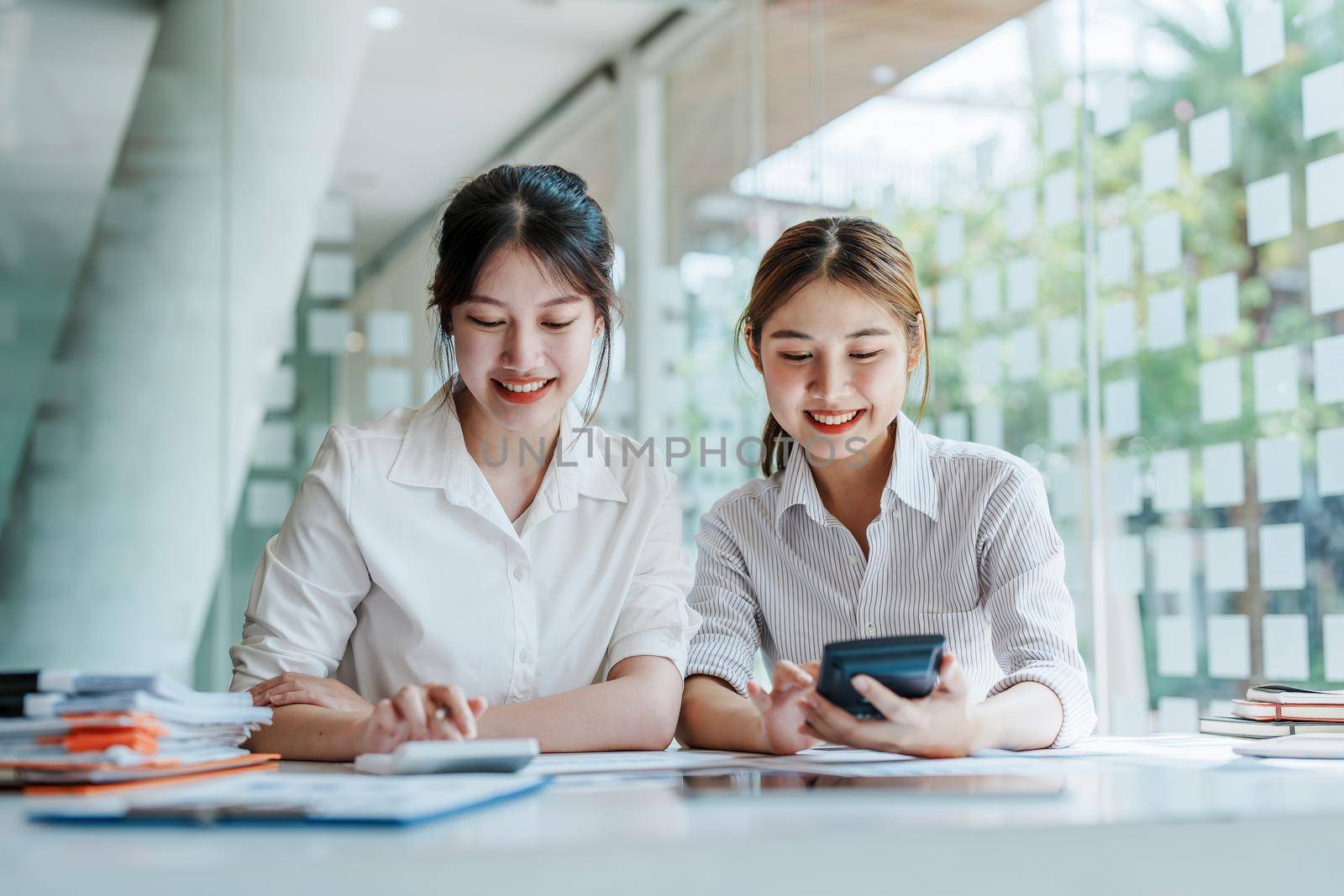 Negotiation, Analysis, Discussion, Portrait of an Asian young economist and marketer pointing to a financial data sheet to plan investments to prevent risks and losses for the company. by Manastrong