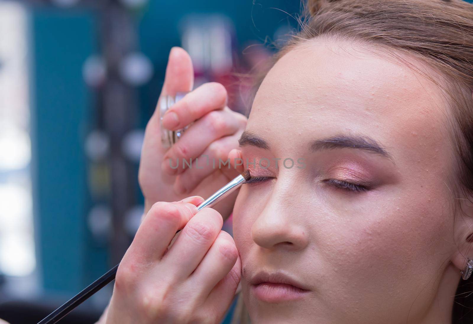 Close-up of a makeup artist's hand with a brush paints the eyelid of a client. Female master makes makeup to a young woman. Business concept - beauty salon, facial skin care, cosmetology.