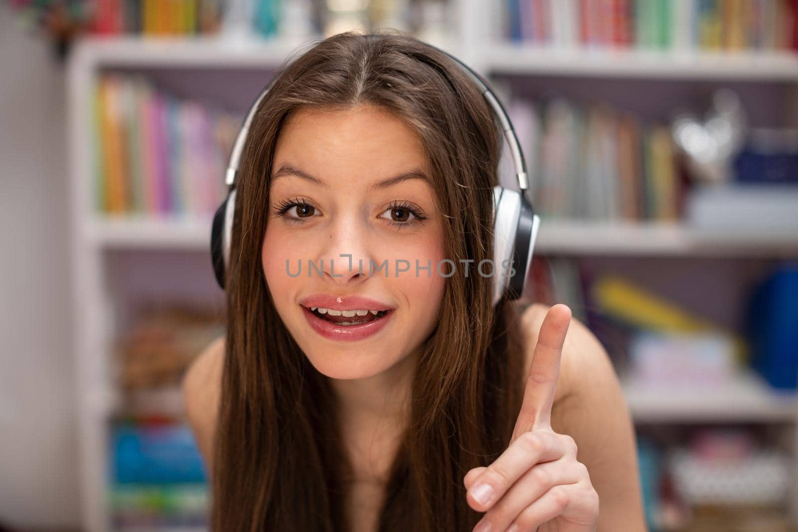 Happy teenage girl with wireless headphones on her ears dry music. Attractive girl with long hair is pointing her finger.