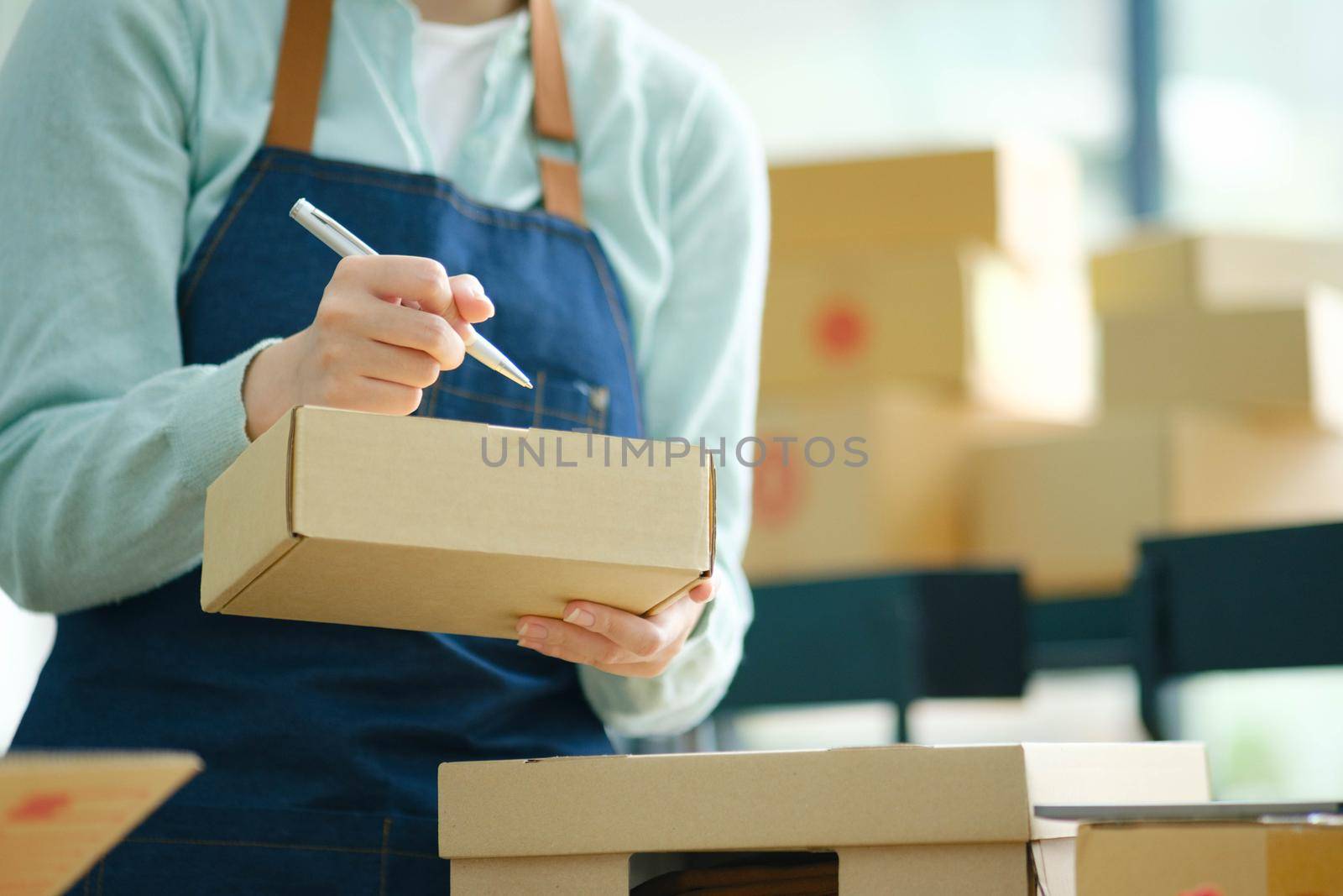 Young Asian businesswoman online store writing customer's address in shipping box.
