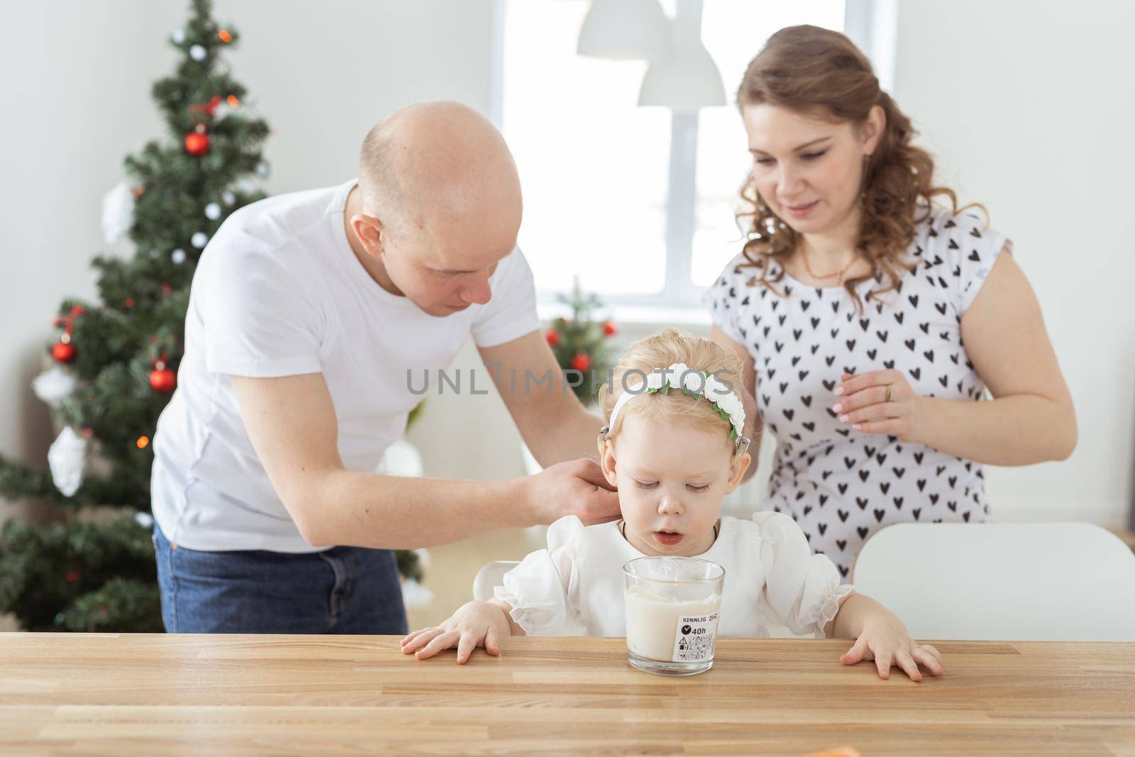 Mother and father helps to put on cochlear implant for their deaf baby daughter in christmas living room. Hearing aid and innovating medical technologies treatment deafness concept by Satura86