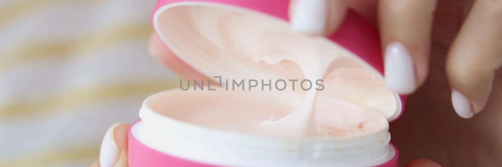 Close-up of lady open pink container with creamy texture inside for skin care. Use moisturizing cream for body and face. Skincare, wellness, beauty concept