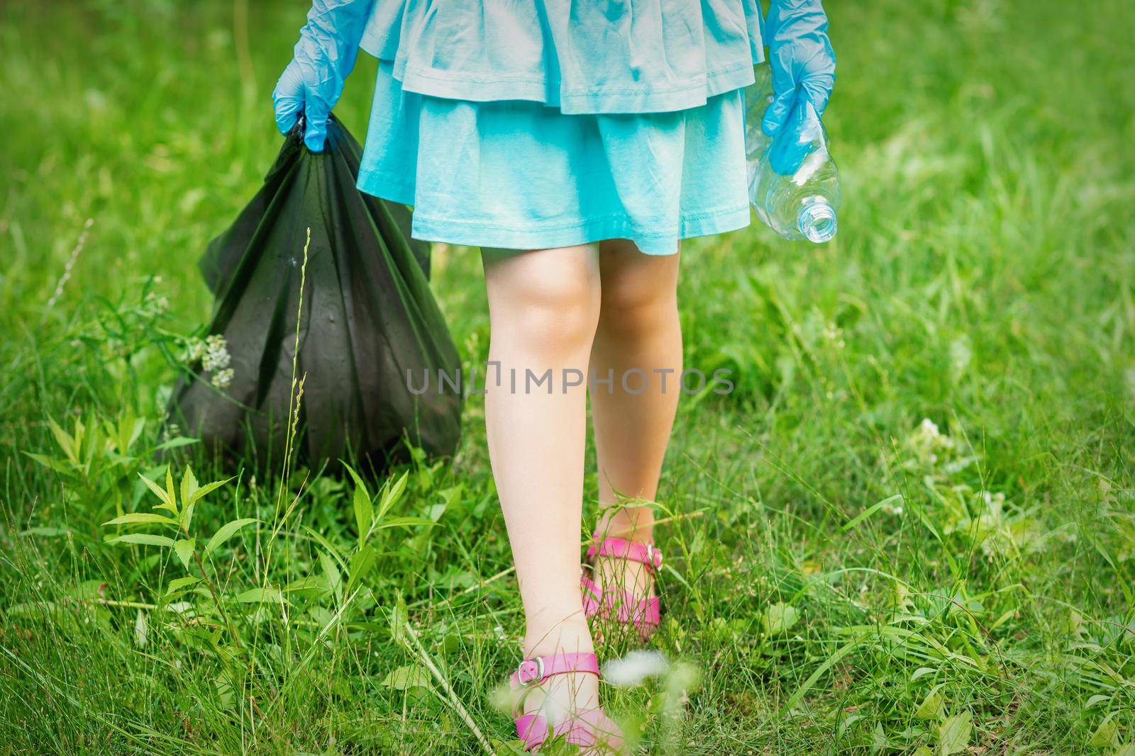 Little girl with crumpled plastic bottle and garbage bag in her hands while cleaning garbage in the park
