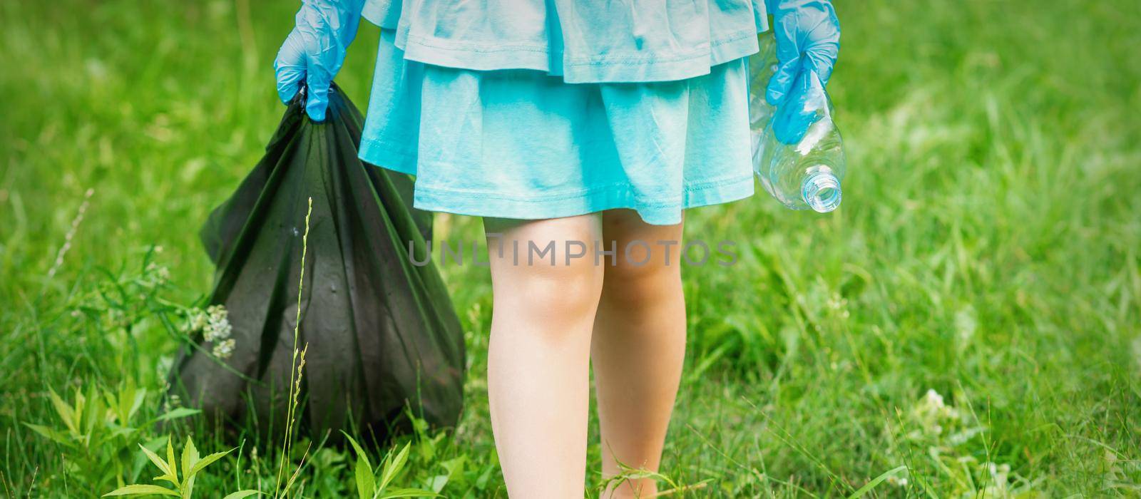 Little girl with crumpled plastic bottle and garbage bag in her hands while cleaning garbage in the park