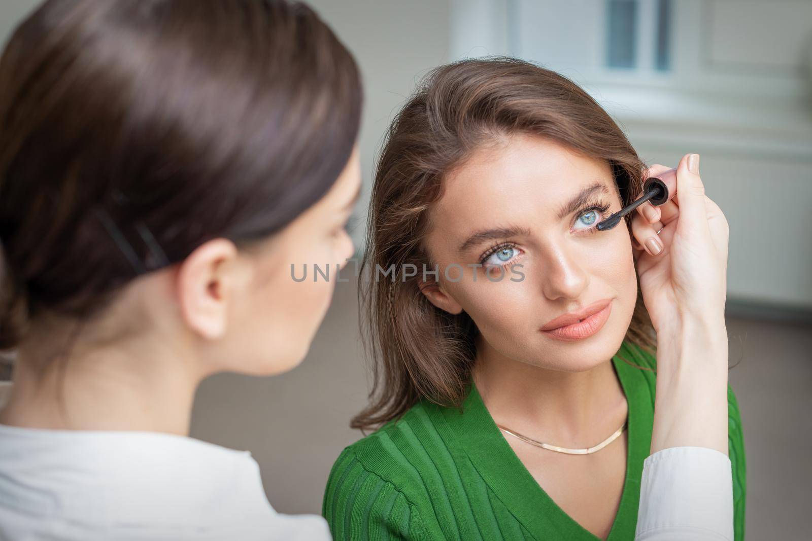 Professional makeup artist applying mascara on lashes of beautiful young caucasian woman in beauty salon