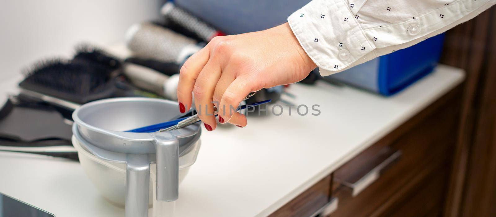 Hand of hairstylist prepares dye in bowl for coloring hair in hairdress salon