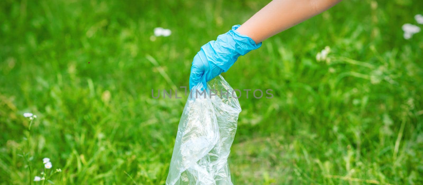 Hand of child cleans the park from plastic debris lying on the green grass
