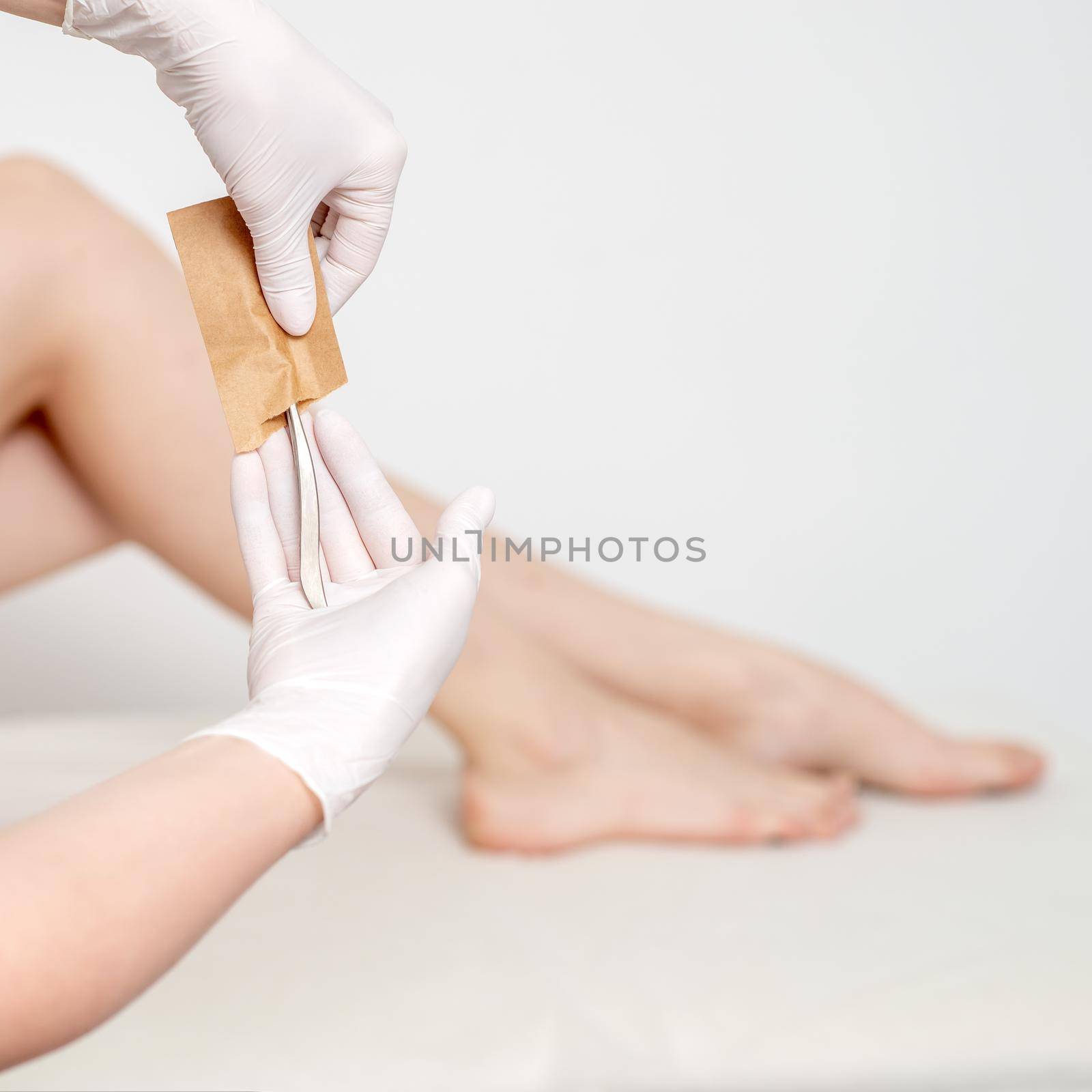 Human hands in protective gloves taking off medical or beauty tools from craft envelope before procedures on background of female legs