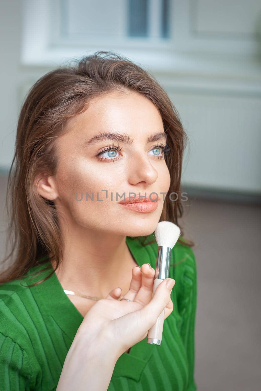 Make up artist applying professional make up of tonal foundation on the face of beautiful young caucasian woman in make up room. Base for make up.