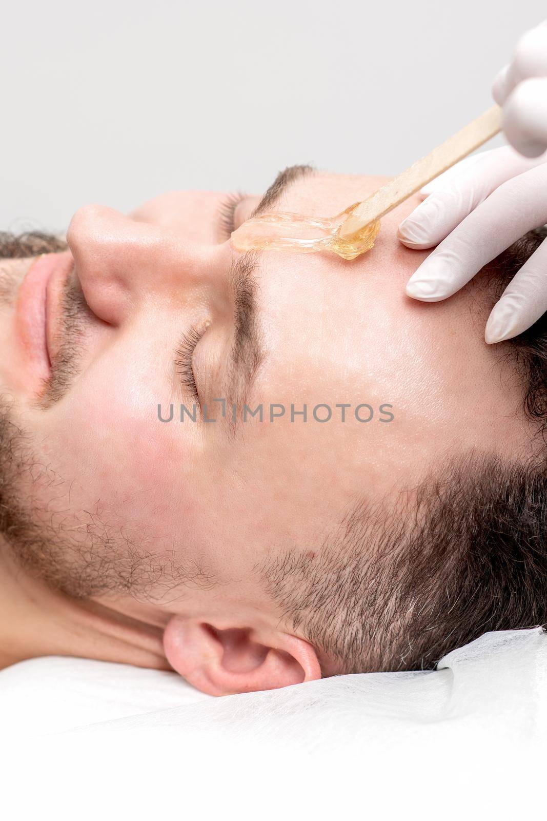 Beautician applies wax between male eyebrows before the procedure of waxing in the beauty salon.