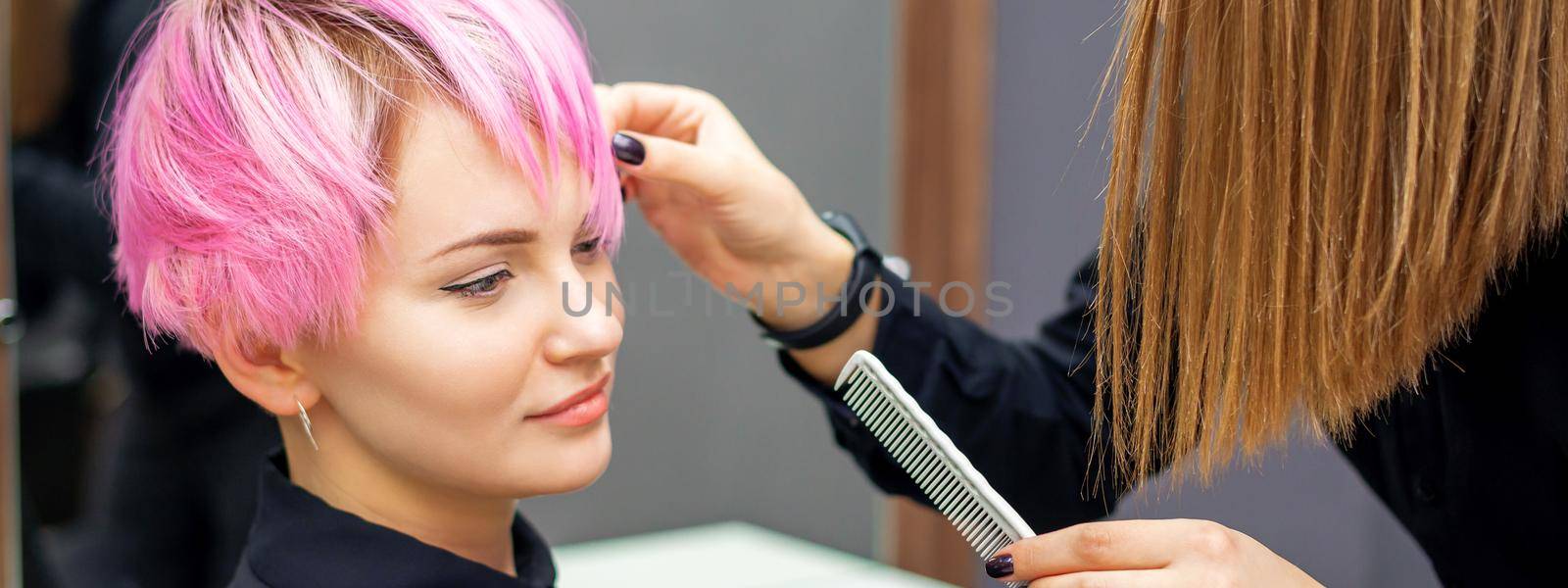 Young woman receiving short pink hairstyle by female hairdresser in beauty salon