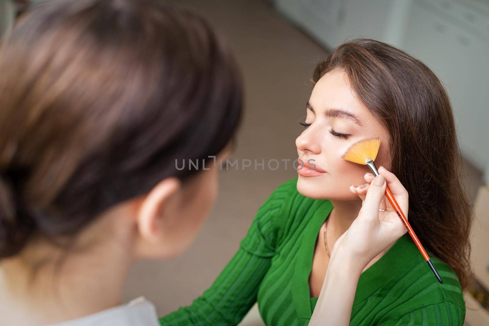 Make up artist applying professional make up of tonal foundation on the face of beautiful young caucasian woman in make up room. Base for make up.