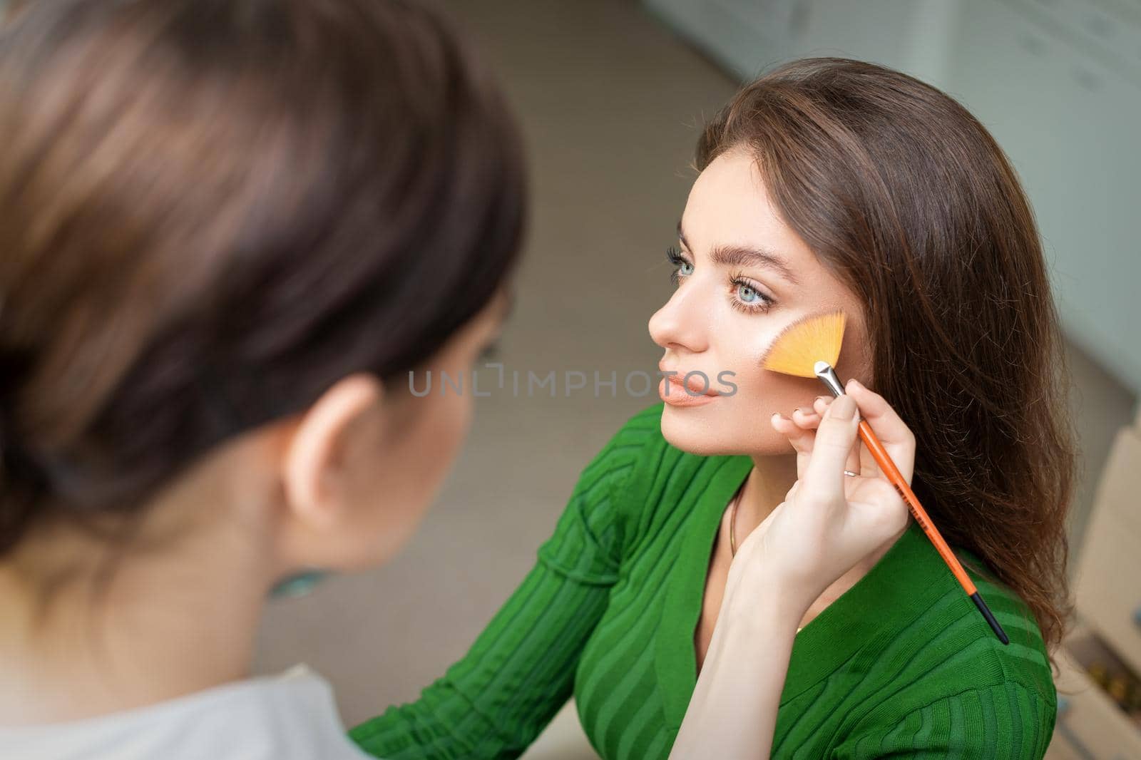 Make up artist applying professional make up of tonal foundation on the face of beautiful young caucasian woman in make up room. Base for make up.