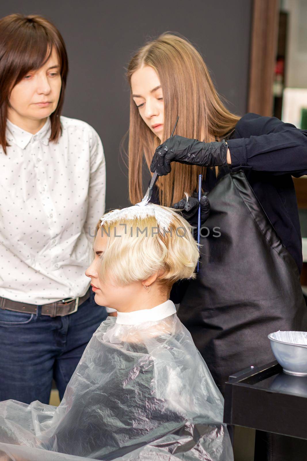 Young female trainee learns to draw women's hair under the supervision of a professional hairdresser in a barbershop