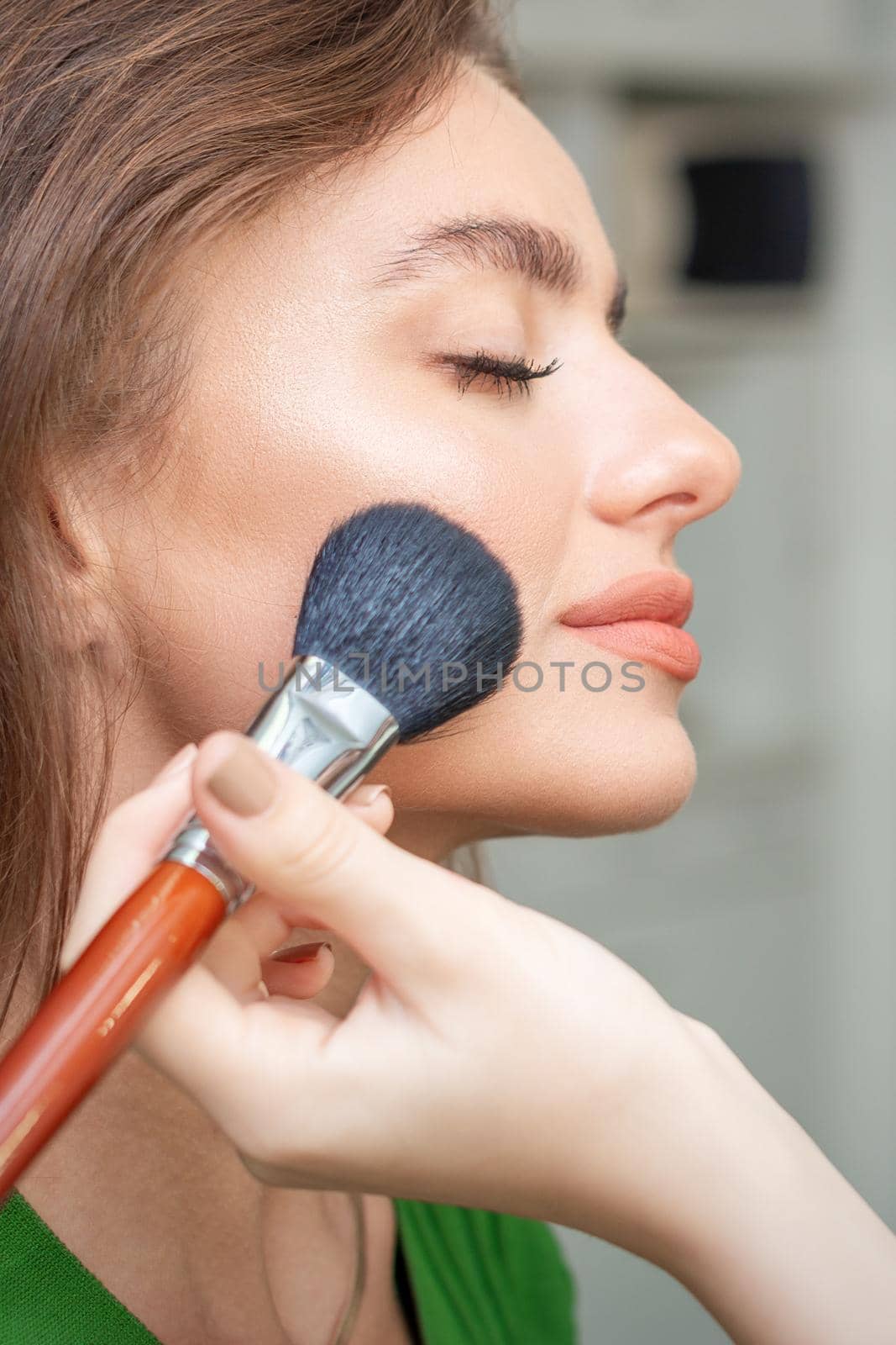 Make up artist applying professional make up of tonal foundation on the face of beautiful young caucasian woman in make up room. Base for make up.