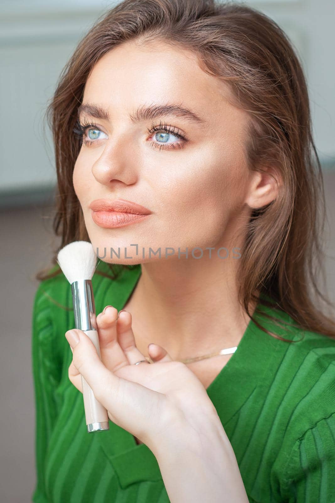 Make up artist applying professional make up of tonal foundation on the face of beautiful young caucasian woman in make up room. Base for make up.