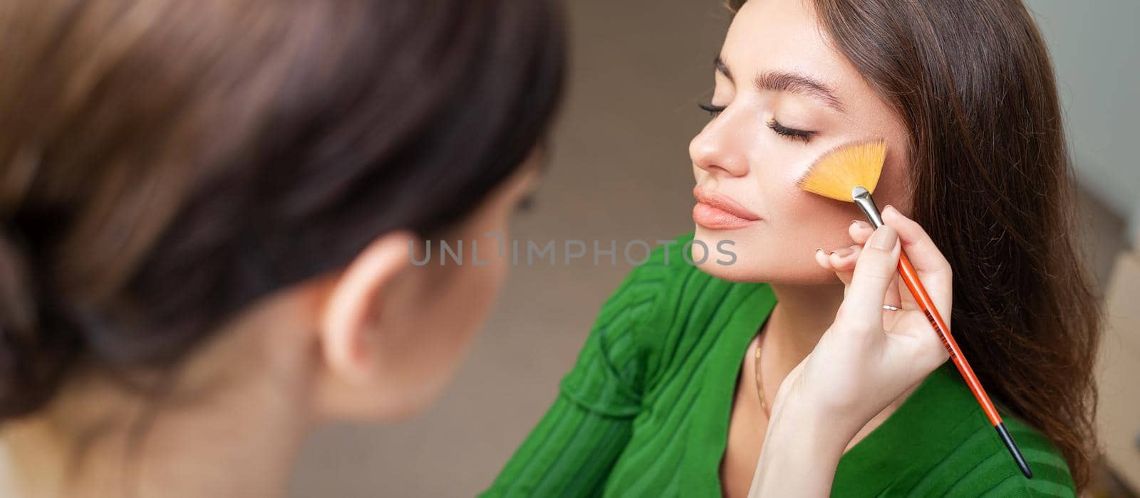 Make up artist applying professional make up of tonal foundation on the face of beautiful young caucasian woman in make up room. Base for make up.