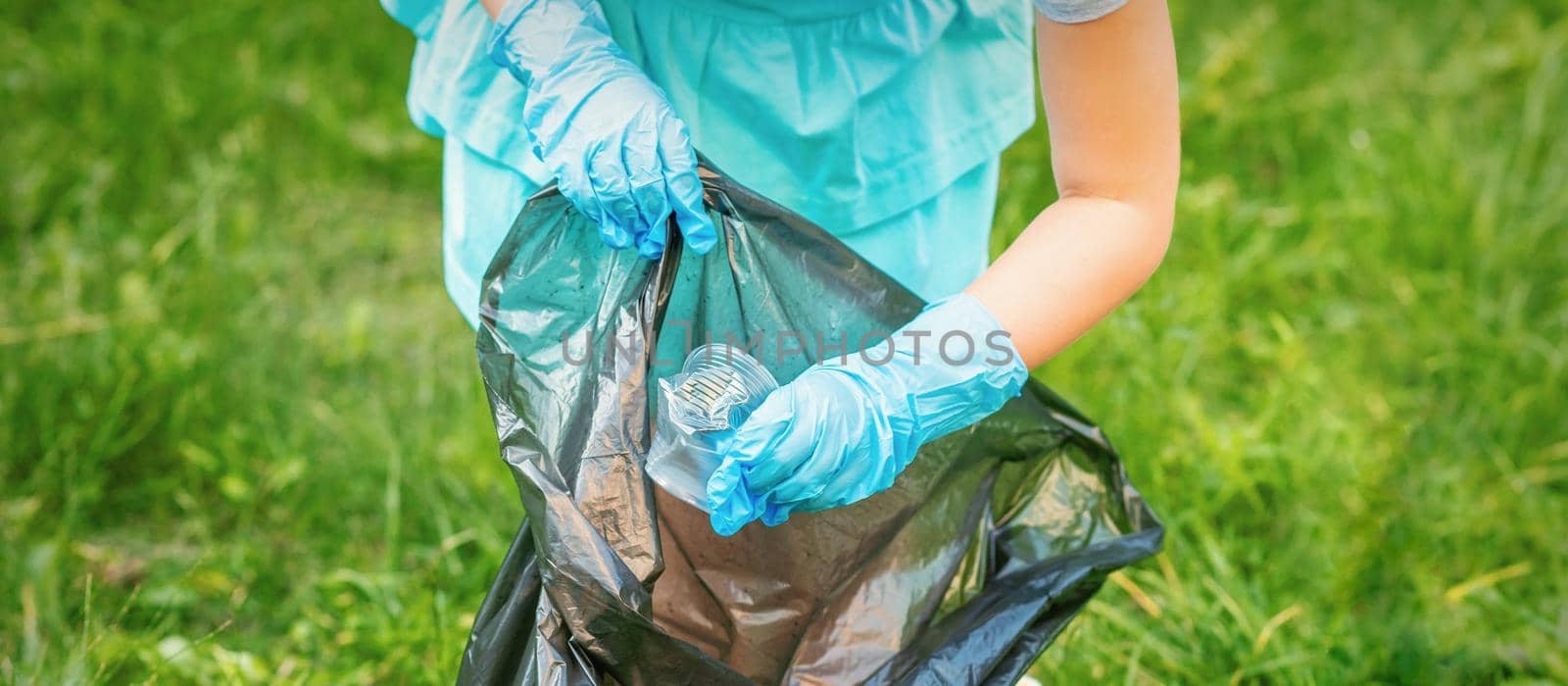 Child collects plastic trash from grass throwing garbage in garbage bag in the park