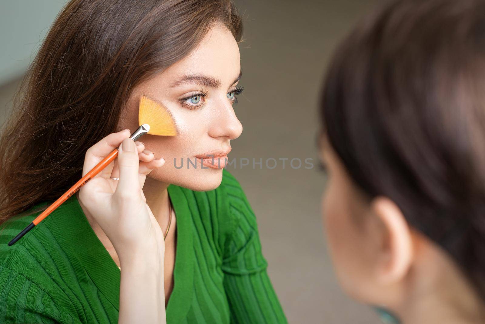 Make up artist applying professional make up of tonal foundation on the face of beautiful young caucasian woman in make up room. Base for make up.