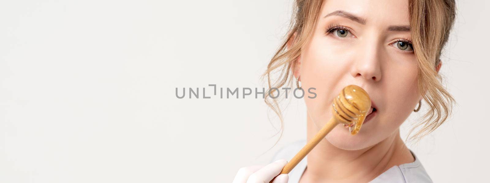 Portrait of beautiful young caucasian woman eating honey with wooden spoon on white background