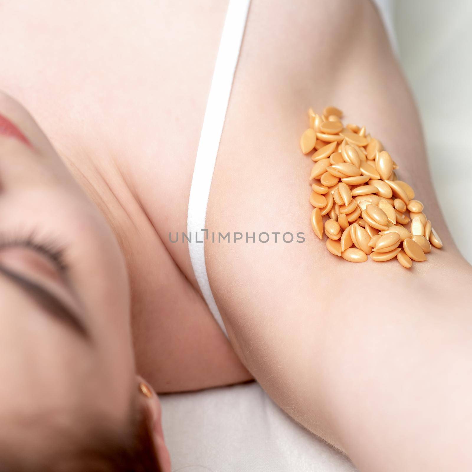 Wax orange beans on armpit of young caucasian woman. Depilation concept