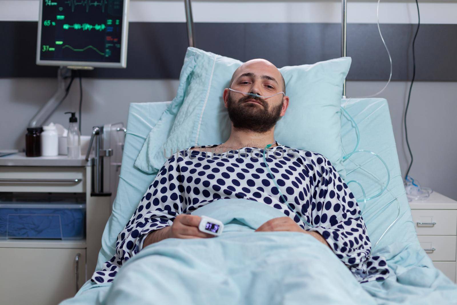 Sick man looking into camera while sitting in bed waiting for disease treatment by DCStudio