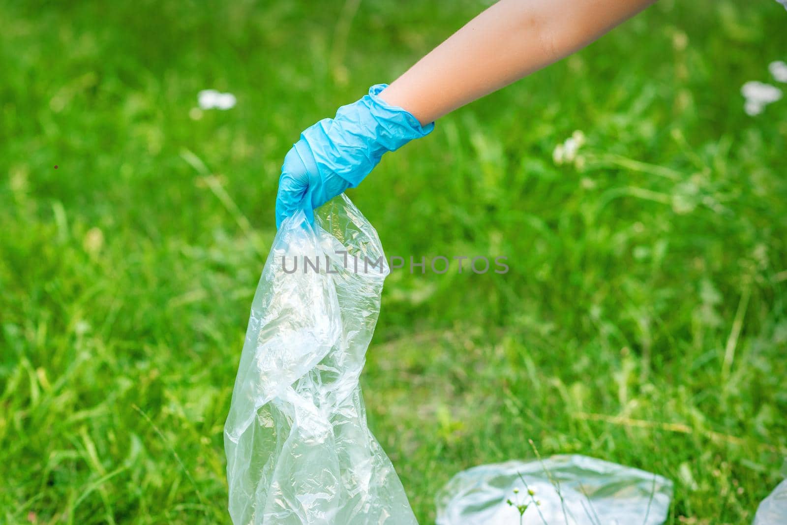 Hand of child cleans the park from plastic debris lying on the green grass