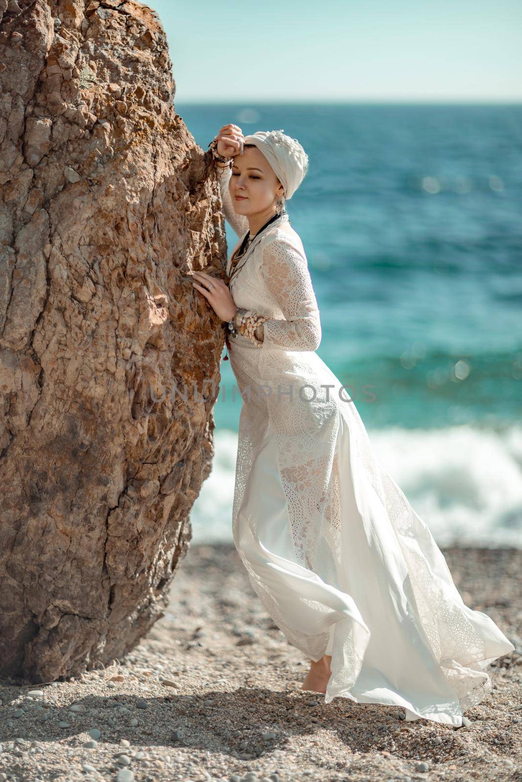 Middle aged woman looks good with blond hair, boho style in white long dress on the beach decorations on her neck and arms