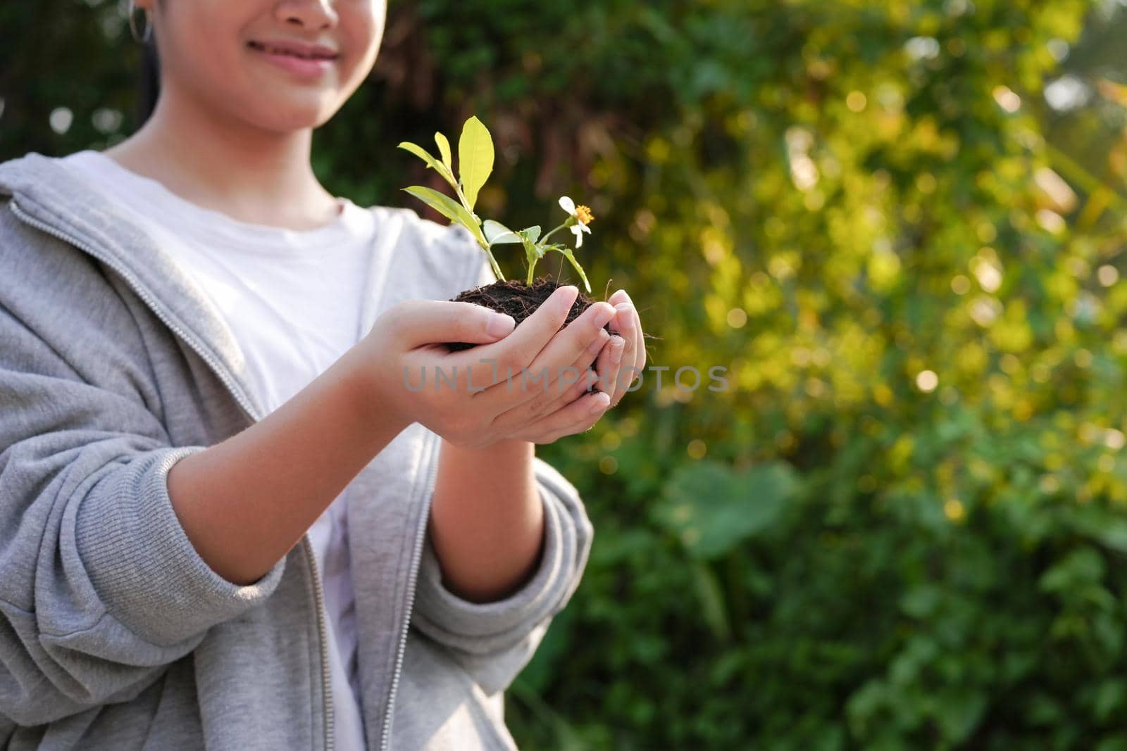 Happy girl with plant in her hand with blurred green nature background. Earth day, environmental concept. by prathanchorruangsak