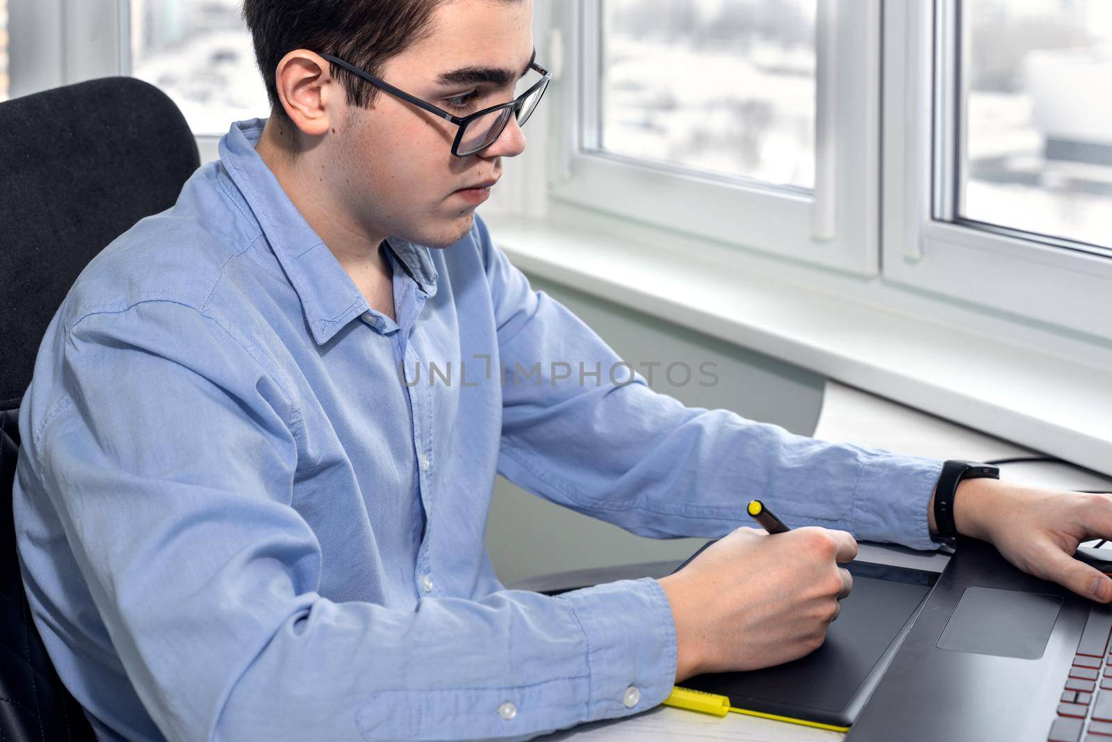 serious young man in glasses as he works on his laptop using a graphics tablet