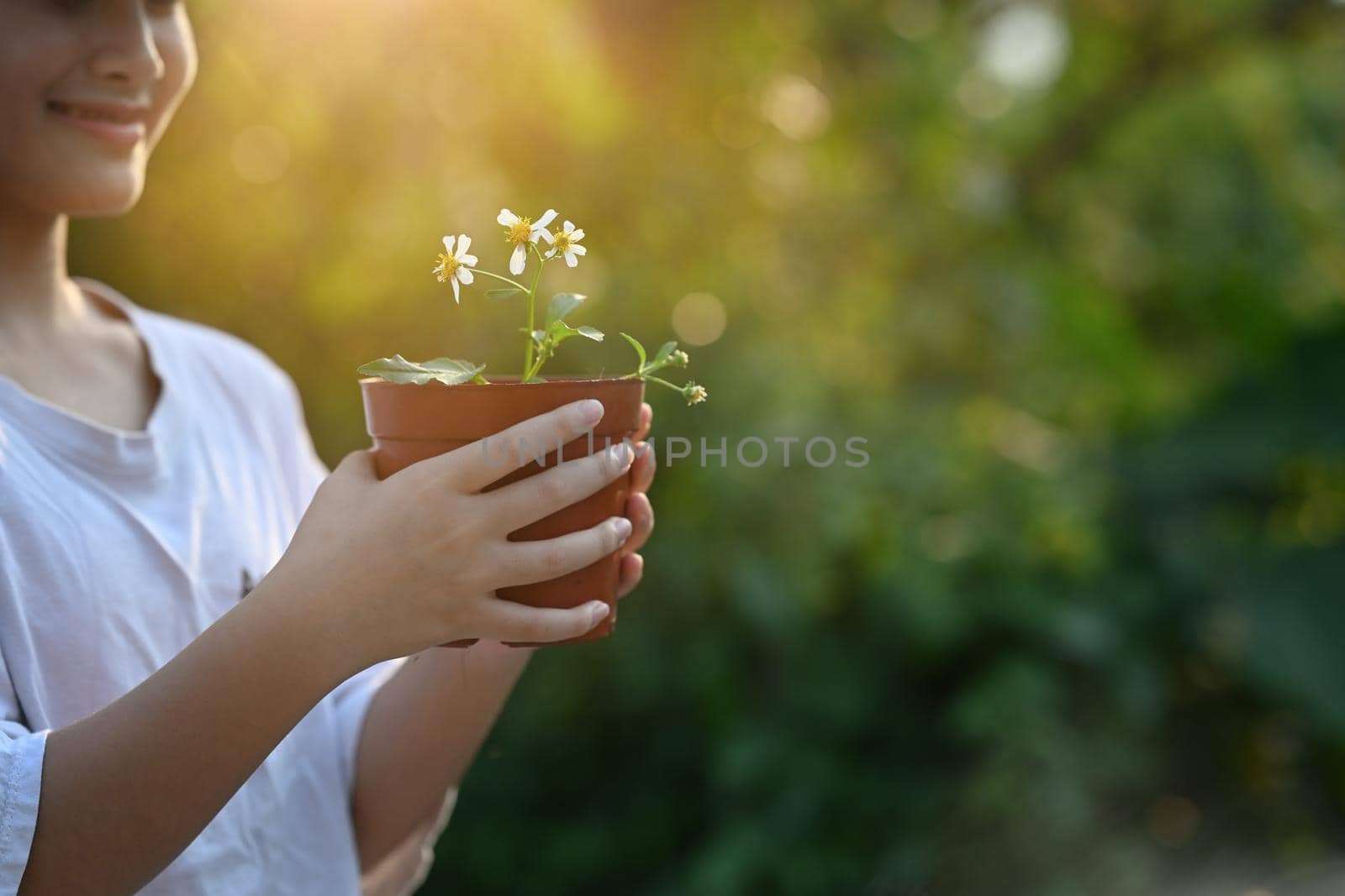 Smiling little girl holding potted plant in hands against blurred green nature background. Earth day, Ecology concept. by prathanchorruangsak