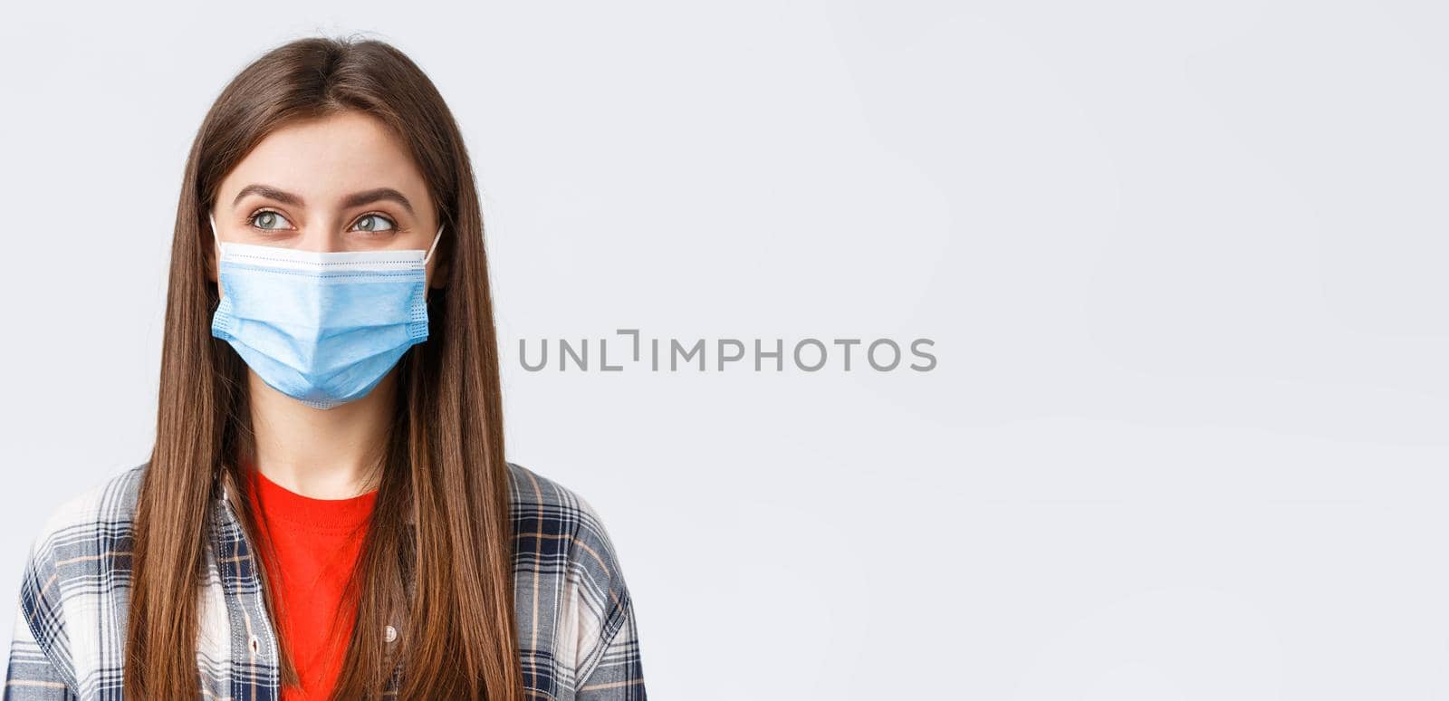 Coronavirus outbreak, leisure on quarantine, social distancing and emotions concept. Close-up of pleased cute girl smiling in medical mask, looking left at pleasant good thing, white background.