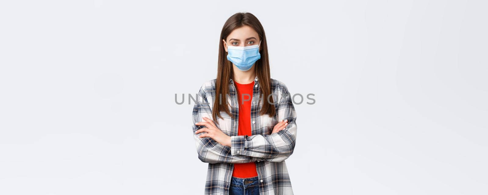 Coronavirus outbreak, leisure on quarantine, social distancing and emotions concept. Confident young woman in checked shirt wear medical mask, cross arms chest, determined look camera.