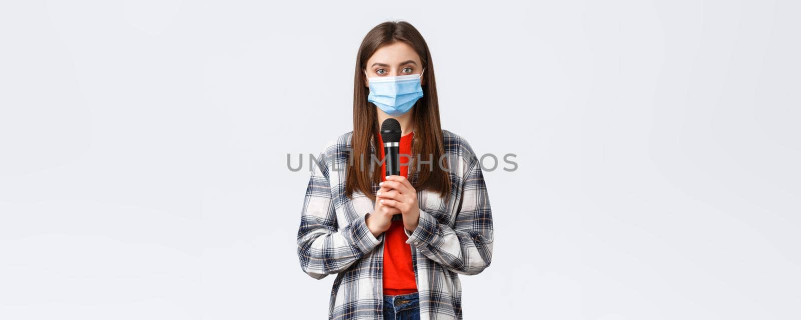 Coronavirus outbreak, leisure on quarantine, social distancing and emotions concept. Girl in medical mask performing song or stand-up, holding microphone want be heard, white background.