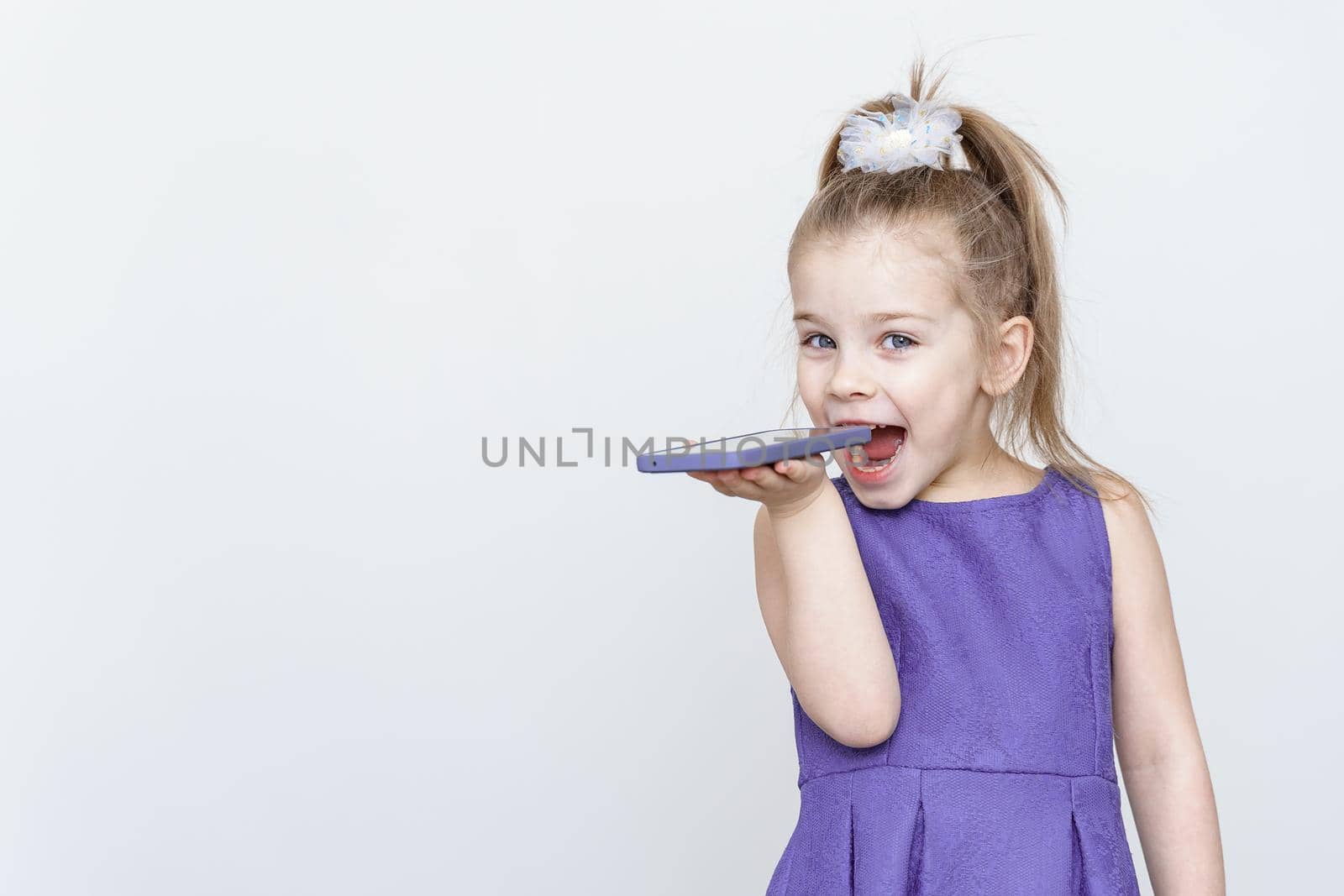 cute playful little girl wants to eat smartphone. place for text, copy space