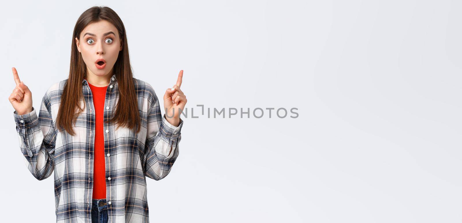 Lifestyle, different emotions, leisure activities concept. Astonished and speechless attractive girl in checked shirt pointing fingers up to tell news, drop jaw staring, make wow expression by Benzoix
