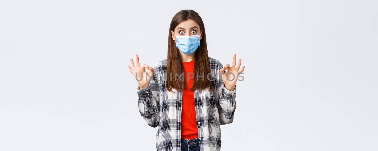Coronavirus outbreak, leisure on quarantine, social distancing and emotions concept. Excited and surprised young woman showing okay sign as see really good promo, wear medical mask.