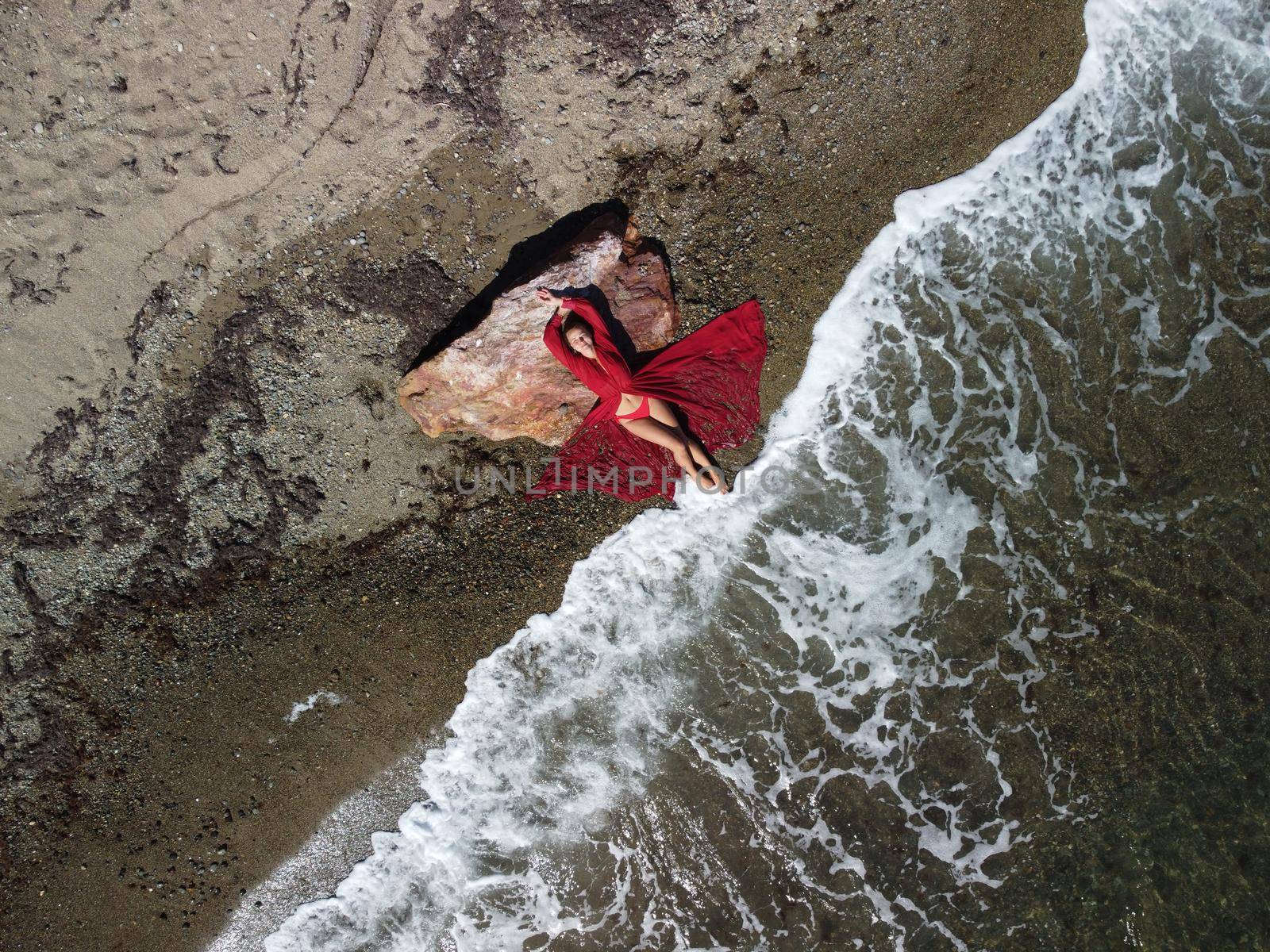 Young sensual blonde woman sitting on the rock near water at sea and enjoys the sea waves on background of two volcanic rocks, like in Iceland. Dreams holidays and weekend vacation in summer time