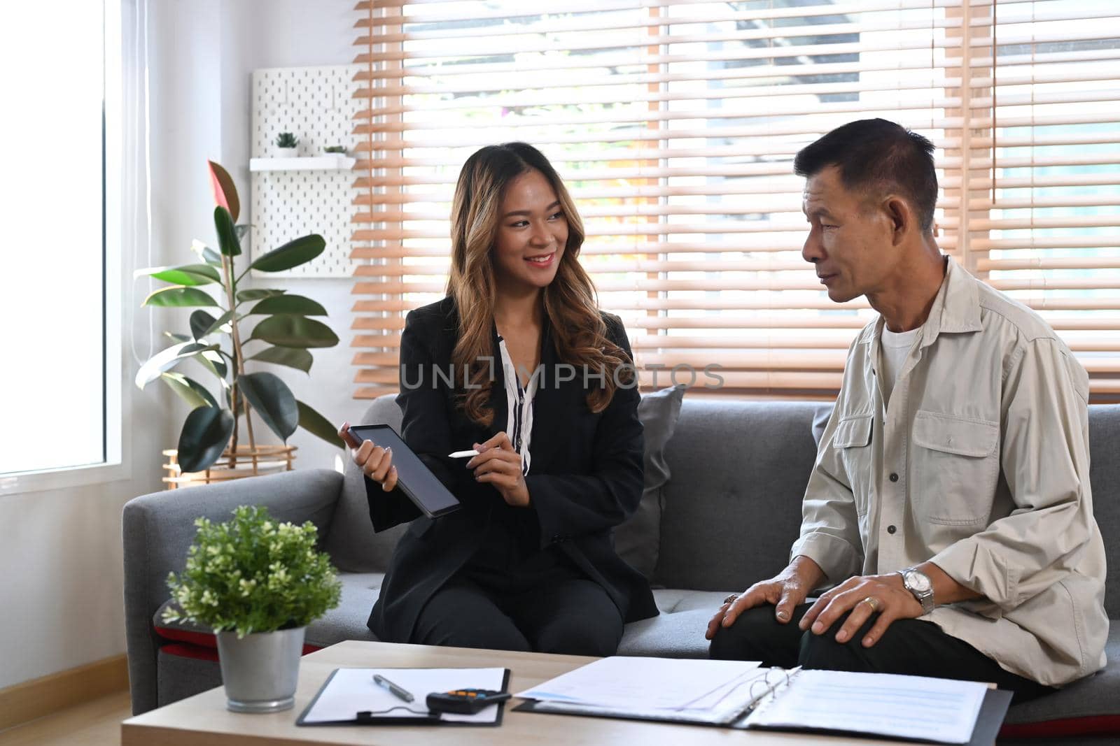 Confident female agent holding digital tablet and explaining medical health insurance for elderly man.