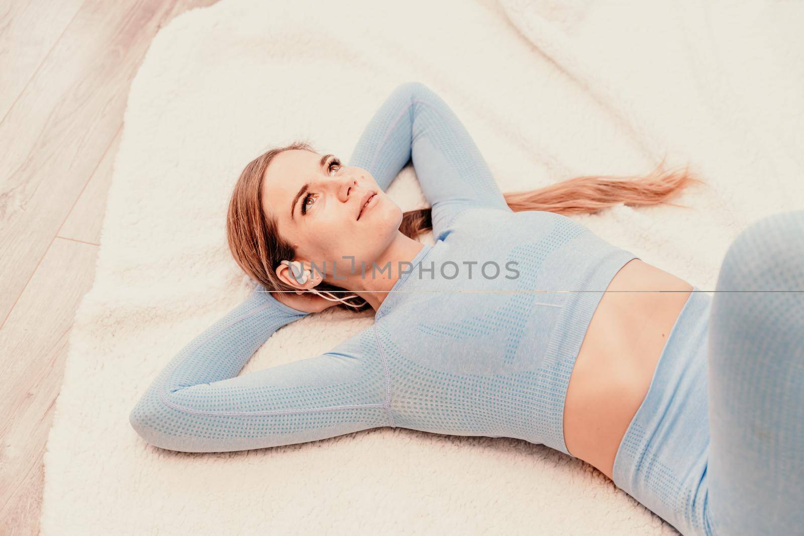 Top view portrait of relaxed woman listening to music with headphones lying on carpet at home. She is dressed in a blue tracksuit