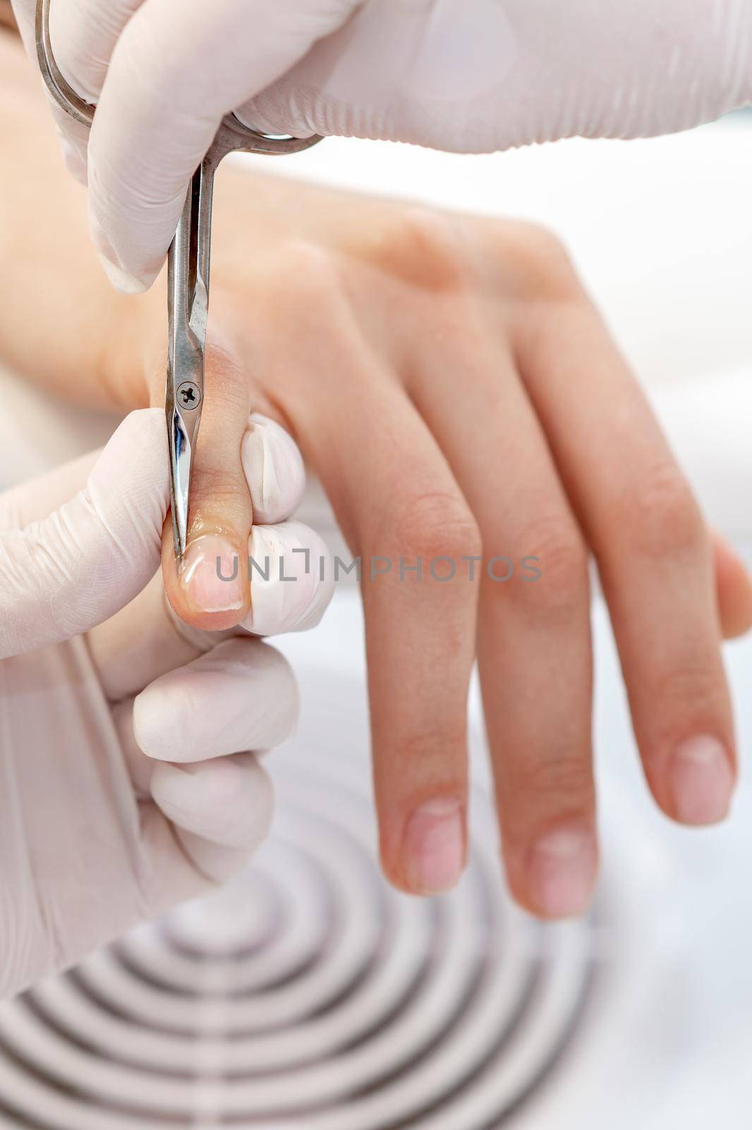 Close up of manicurist using manicure scissors to remove cuticle of female nails in manicure salon