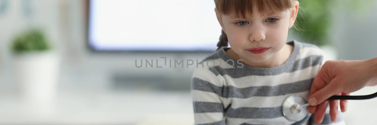 Portrait of girl being examined by pediatrician doctor with stethoscope. Calm kid sit in office and get checkup. Medicine, appointment concept. Copy space